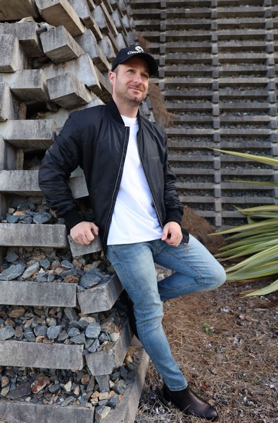 Male model wearing black jacket and cap leaning on the wall