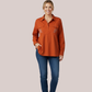 Woman in a burnt orange long-sleeve customizable breastfeeding shirt, featuring a quarter-button placket, twin chest pockets, and white custom leaf-patterned embroidery on the chest.