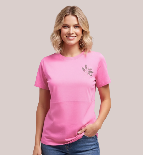 Model wearing a bright pink short-sleeve customizable maternity top with a lift-up panel and subtle custom grey and white leaf-patterned embroidery.