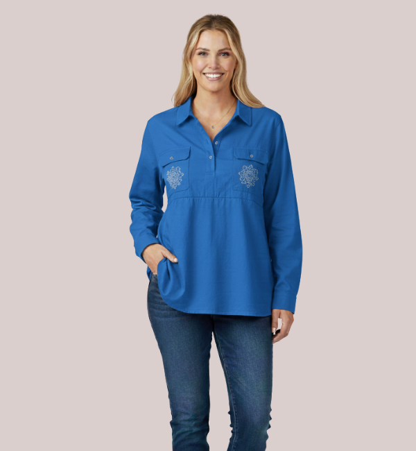 Woman in a vibrant royal blue long-sleeve customizable nursing top with a half-button placket and intricate white custom mandala-style embroidery detail on the chest.