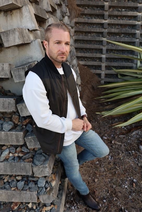 Male model wearing black vest leaning on the wall